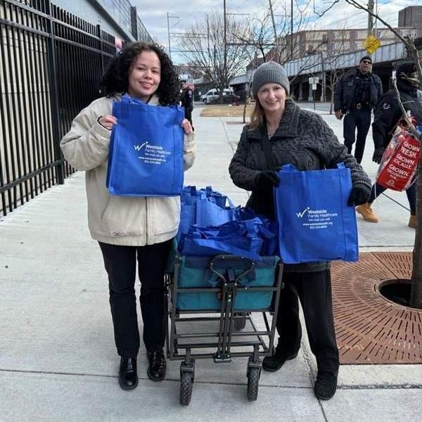Two volunteers holding blue Westside tote bags outdoors